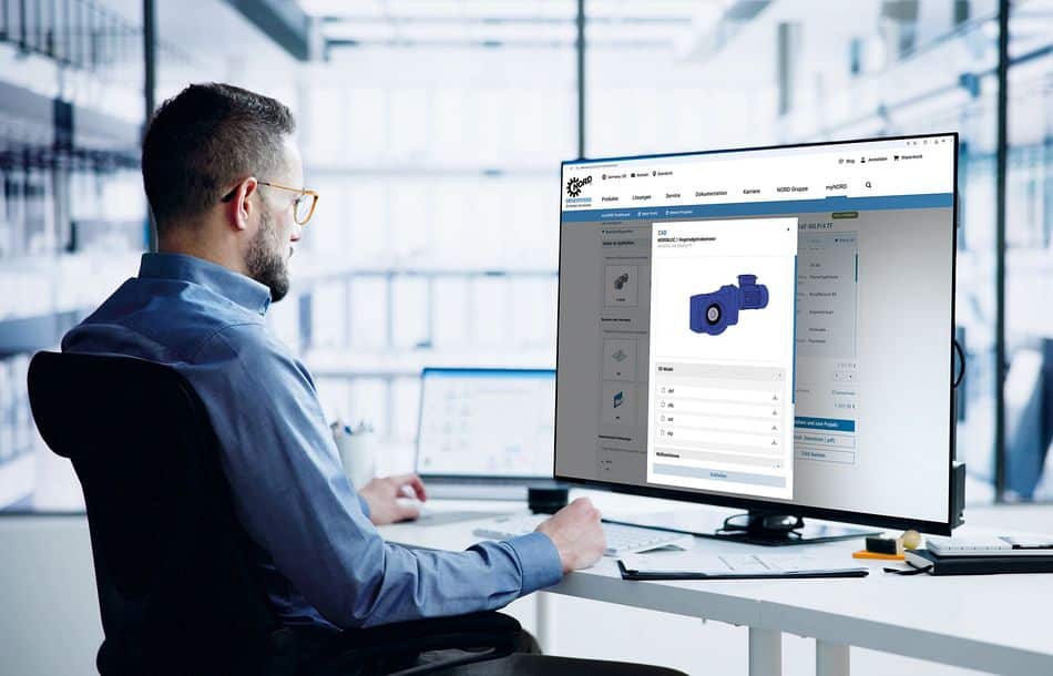 Das Kundenportal von Nord Drivesystems hat neue Funktionen erhalten für eine noch einfachere Konfiguration und Bestellung von Antriebskomponenten Männliche Person in Büro an einem Schreibtisch mit großem Bildschirm, auf dem das überarbeitete Kundenportal My Nord geöffnet ist (im Zentrum ist ein dunkelblauer Getriebemotor zu erkennen), über das Antriebskomponenten des Herstellers konfiguriert und bestellt werden können